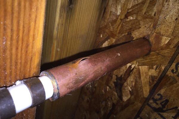 Copper pipe with a noticeable crack surrounded by wooden and plywood surfaces, causing water damage.