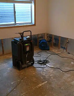 Flood water damage restoration in a room with drying equipment and exposed walls.
