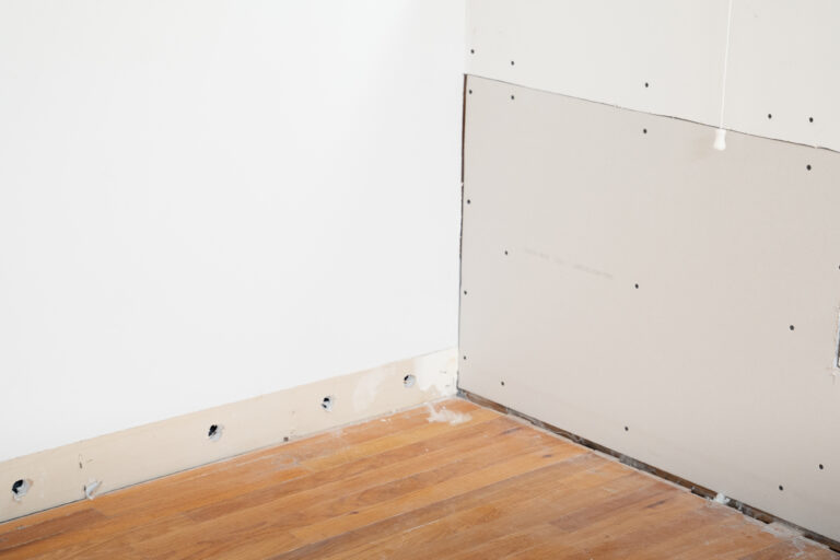 New drywall panel installed beside a wall with drying holes along the base