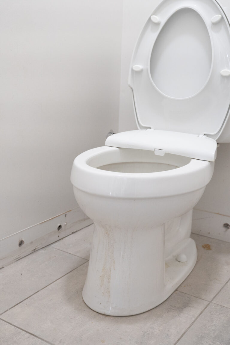 Drilled drying holes along the wall base behind a toilet with the baseboard removed